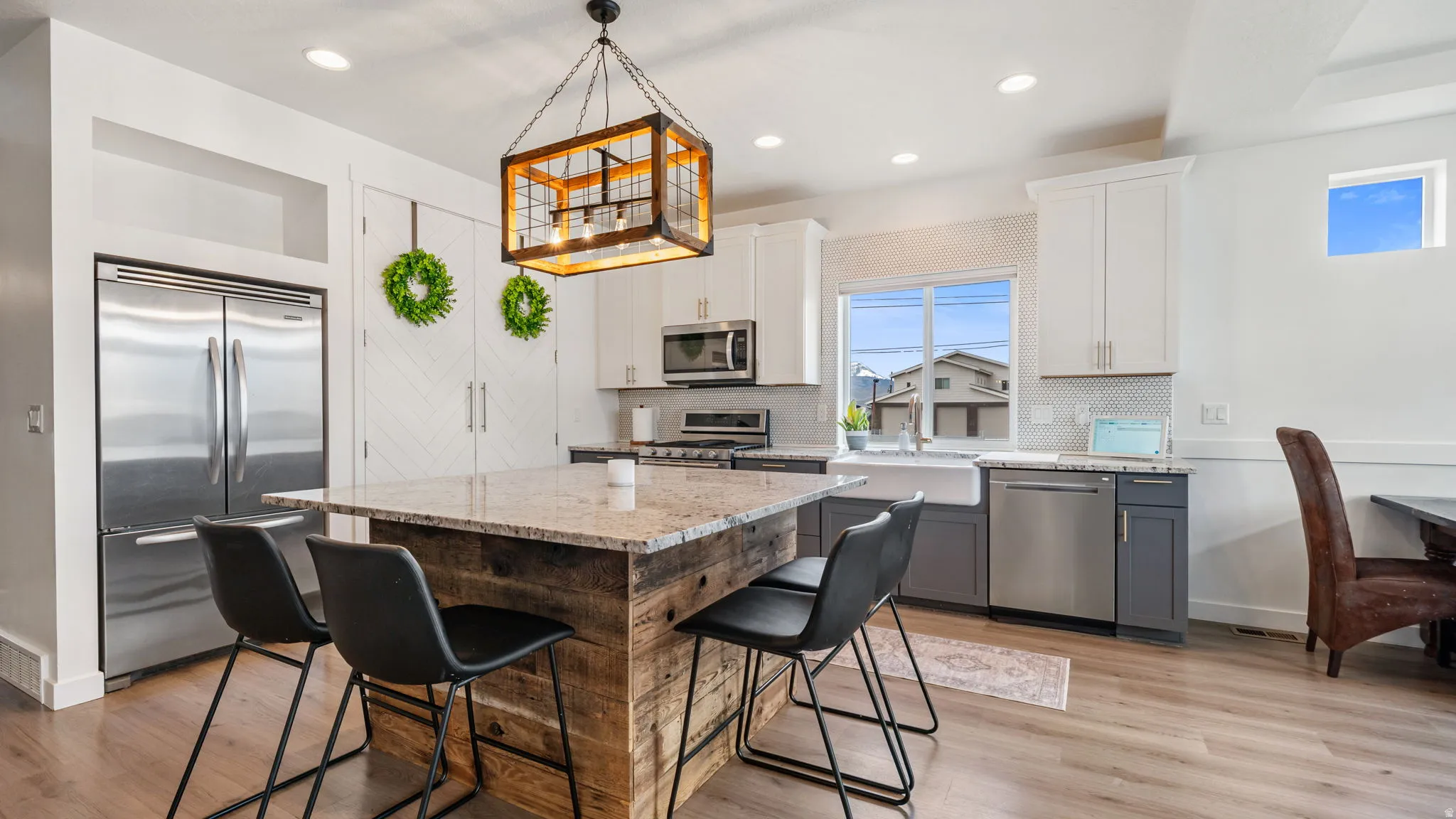Spacious kitchen featuring a rustic wood-finish island with a light-toned countertop, stainless steel appliances, white shaker upper cabinetry, two-tone lower cabinetry, and wood-finish flooring