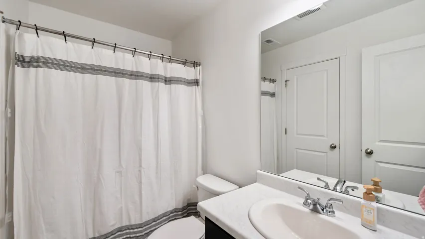 Bathroom featuring a shower with a curtain rod, a toilet, a vanity with an integrated sink, a chrome faucet, and a large wall-mounted mirror