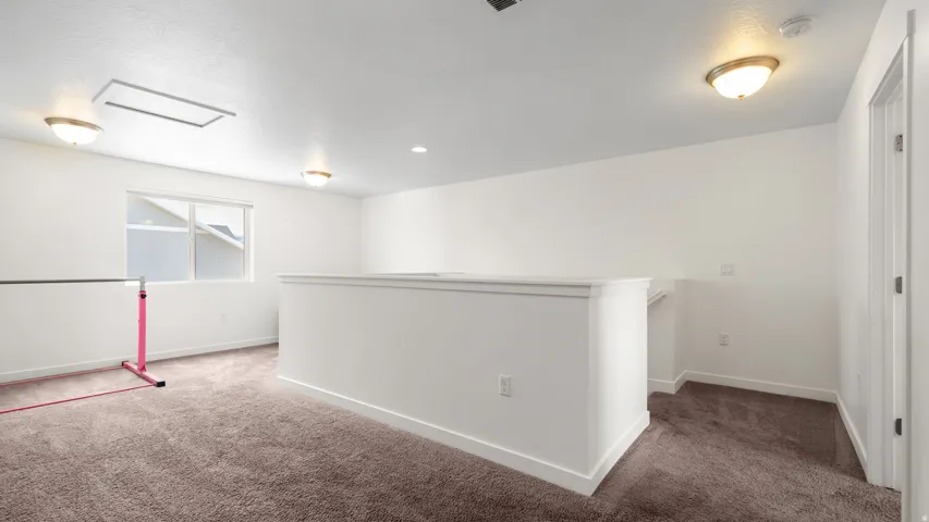 Carpeted loft area featuring a half-wall railing, recessed lighting, and a single window