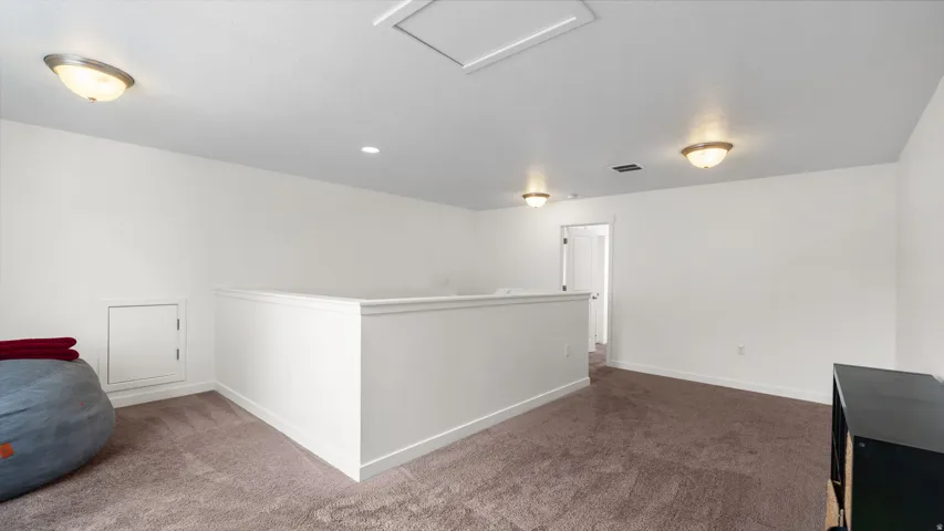 Spacious loft area featuring neutral carpeting and white wall finishes