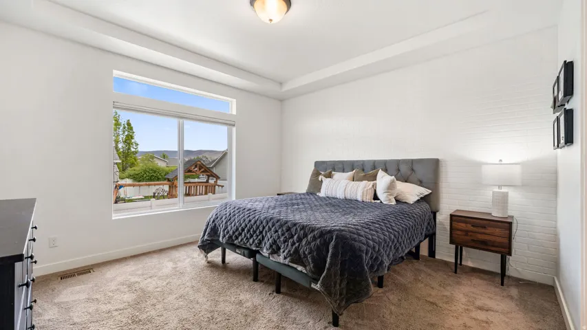 Spacious master bedroom featuring a large window with transom, tray ceiling, textured accent wall, and plush carpeting