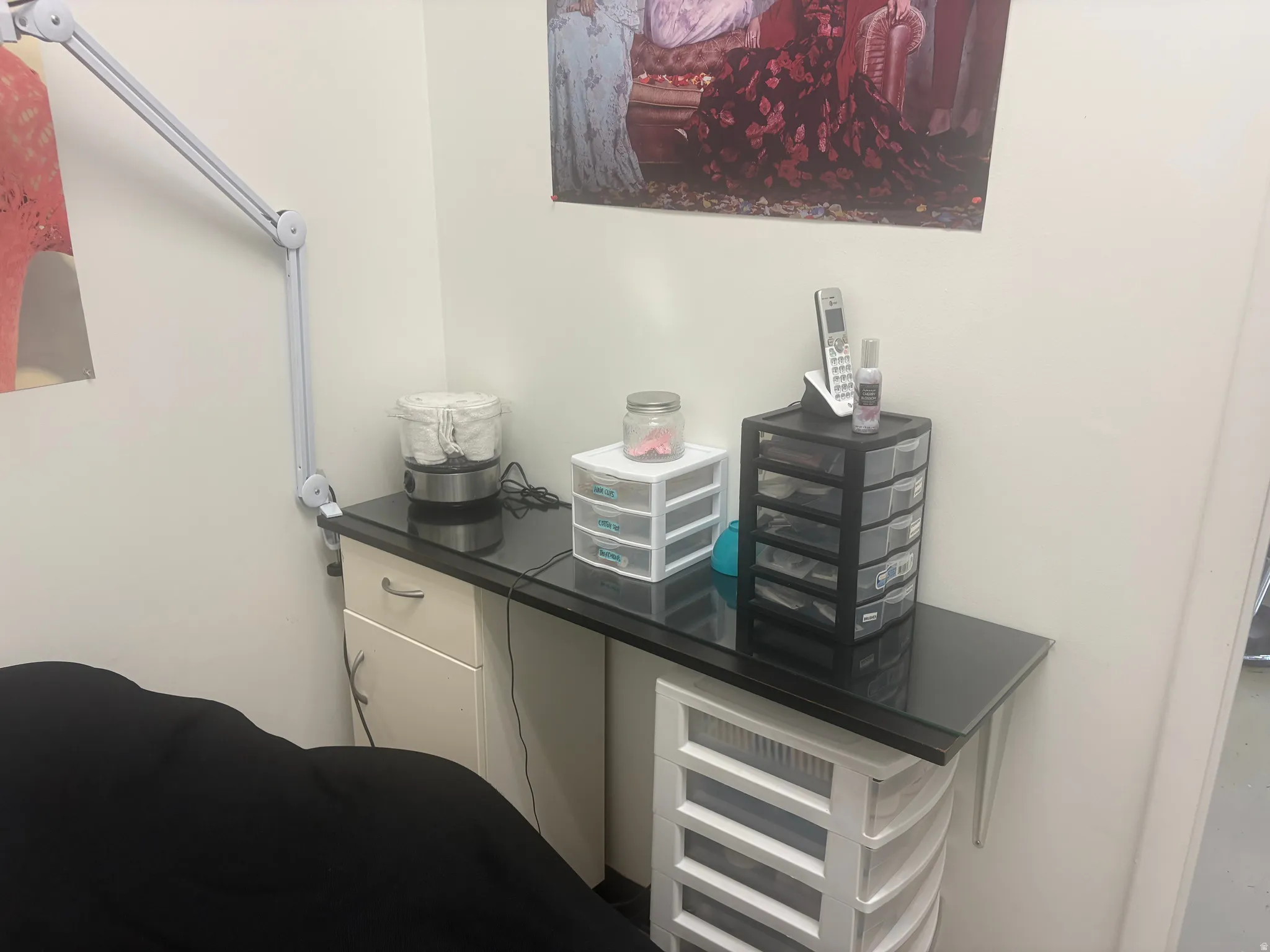 Integrated wall-mounted desk featuring a sleek black countertop, white base cabinetry with a single drawer and storage cabinet, and a multi-jointed wall lamp