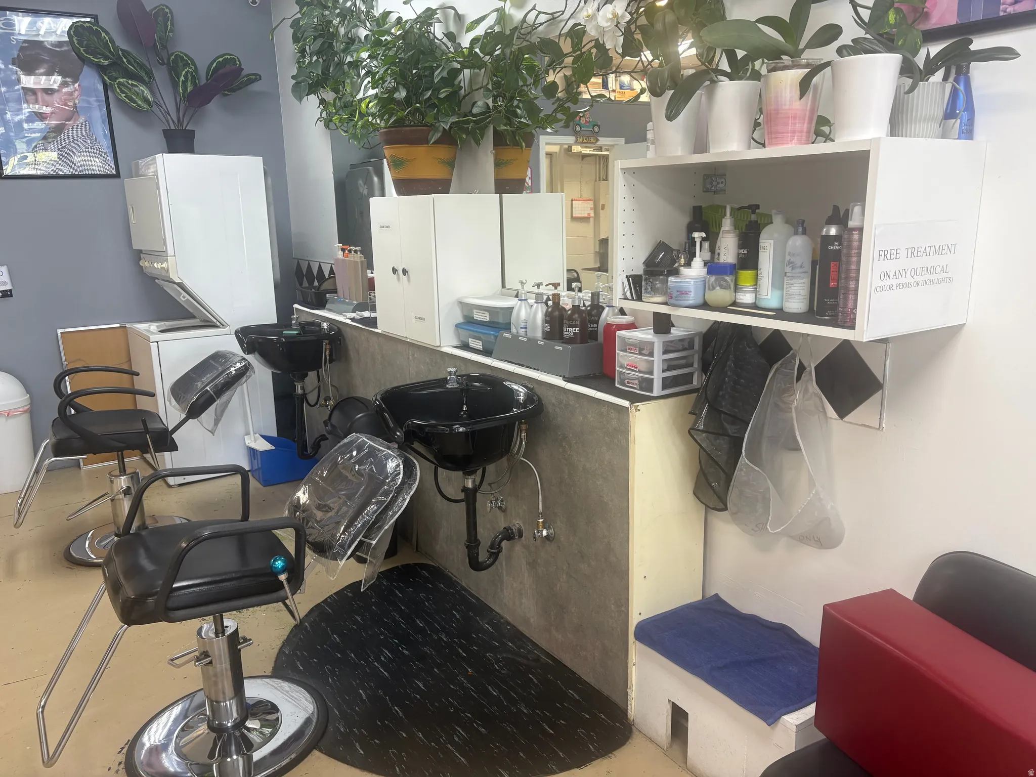 Salon workstation featuring two black basin sinks, dedicated shelving, and light wood-finish flooring