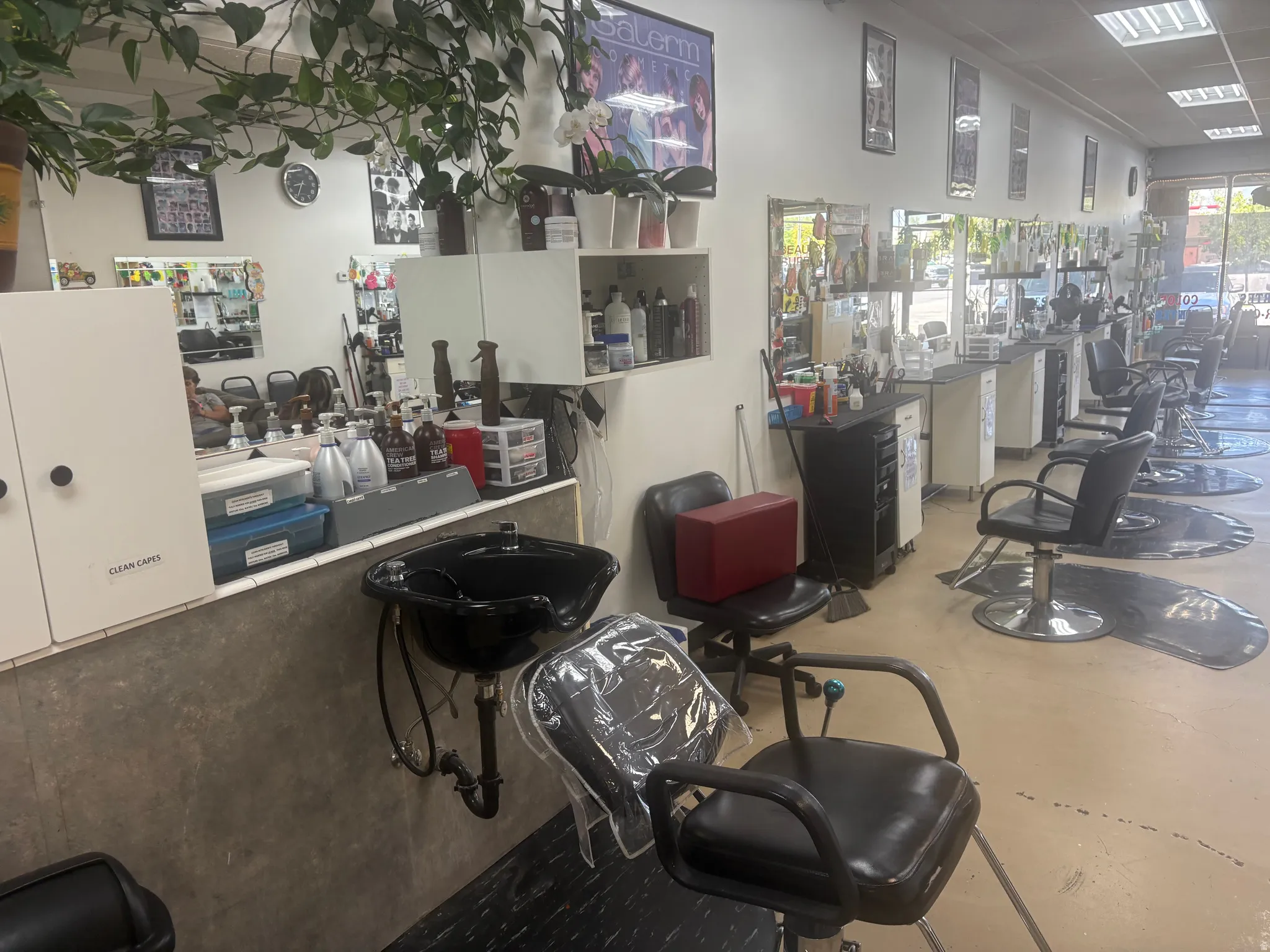 Commercial interior featuring multiple salon stations with individual mirrors and chairs, a wash sink station with a dark basin, recessed ceiling lighting, and light-colored flooring