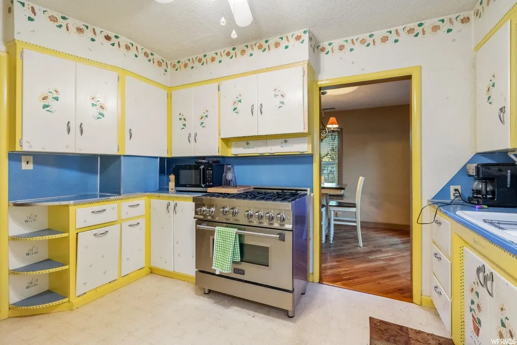 Kitchen featuring stainless steel stove, white cabinets, light floors, black microwave, and a textured ceiling