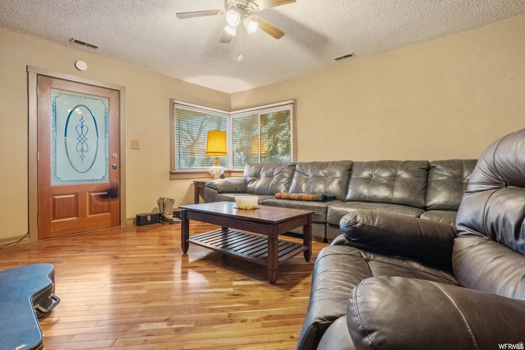 Living area with light wood finished floors, ceiling fan, and a textured ceiling