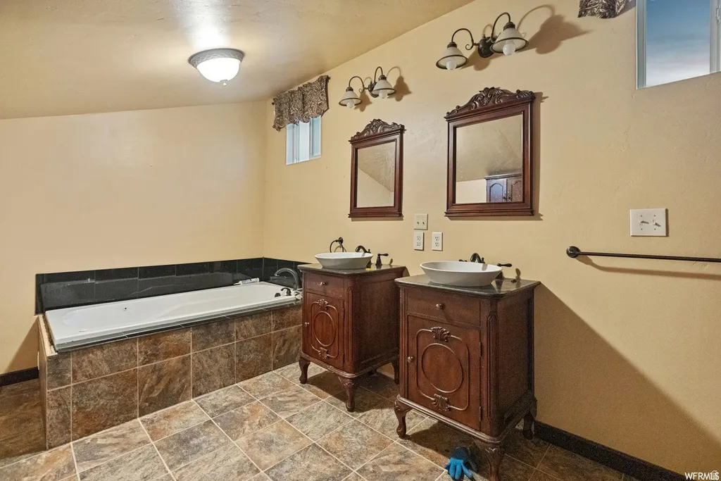 Bathroom featuring two vanities, a bath, and dark stone finish flooring