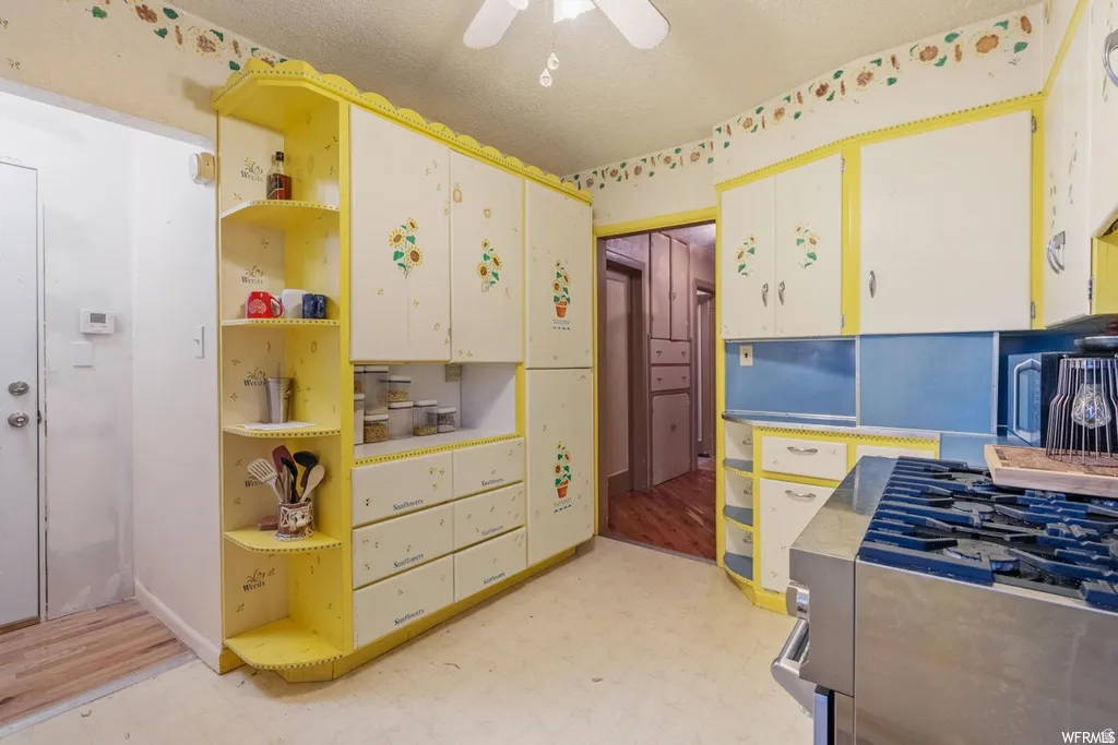 Kitchen with light flooring, gas stove, light countertops, open shelves, and a ceiling fan