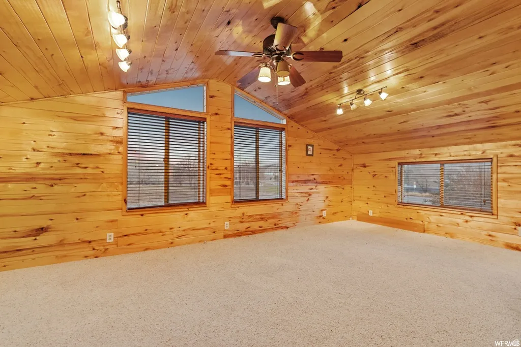 Carpeted spare room featuring track lighting, wooden walls, ceiling fan, and wood ceiling