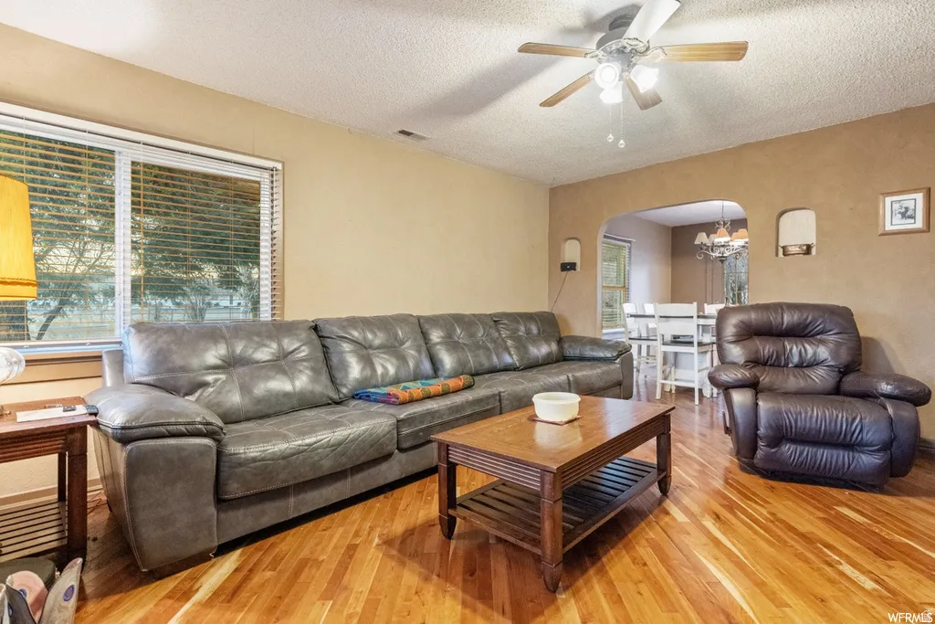 Living room featuring arched walkways, a textured ceiling, ceiling fan, light wood-style flooring, and hanging lights