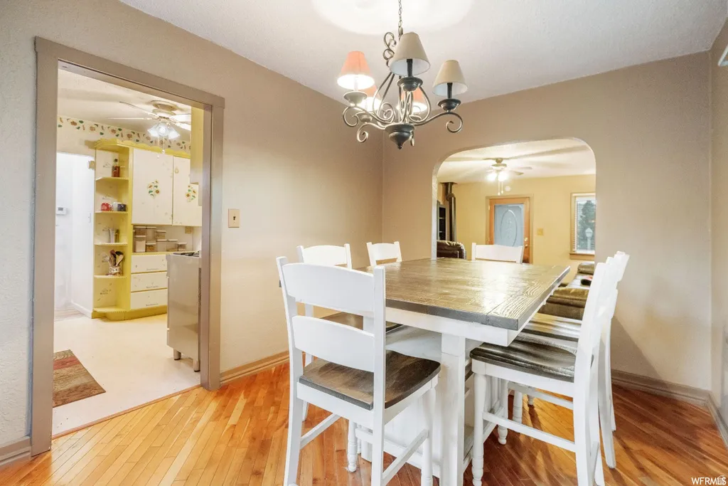 Dining room featuring a ceiling fan, arched walkways, a chandelier, and light wood-style floors