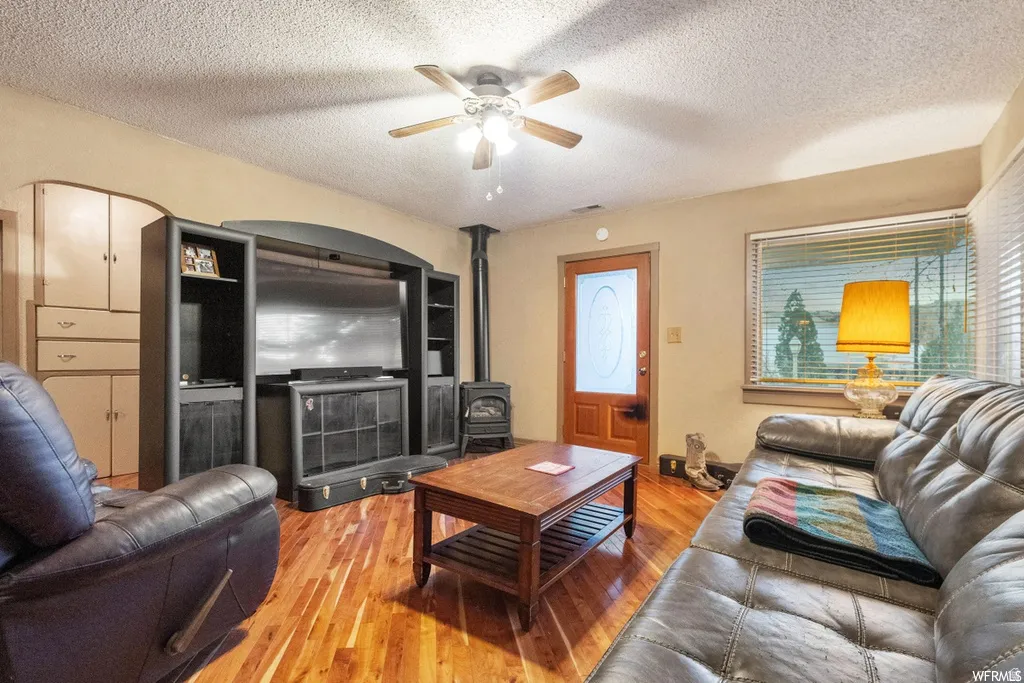 Living area with light wood-style flooring, ceiling fan, a wood stove, and a textured ceiling