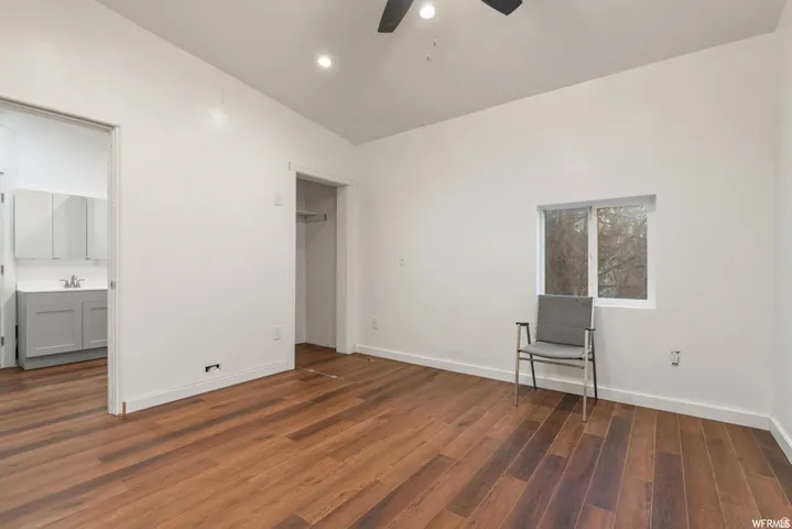 Unfurnished bedroom featuring dark wood-style floors, lofted ceiling, ceiling fan, and ensuite bathroom