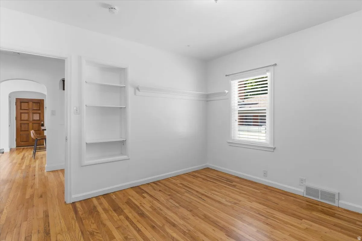 Bright room featuring wood-finish flooring, a white window with horizontal blinds, built-in shelving, and white wall molding