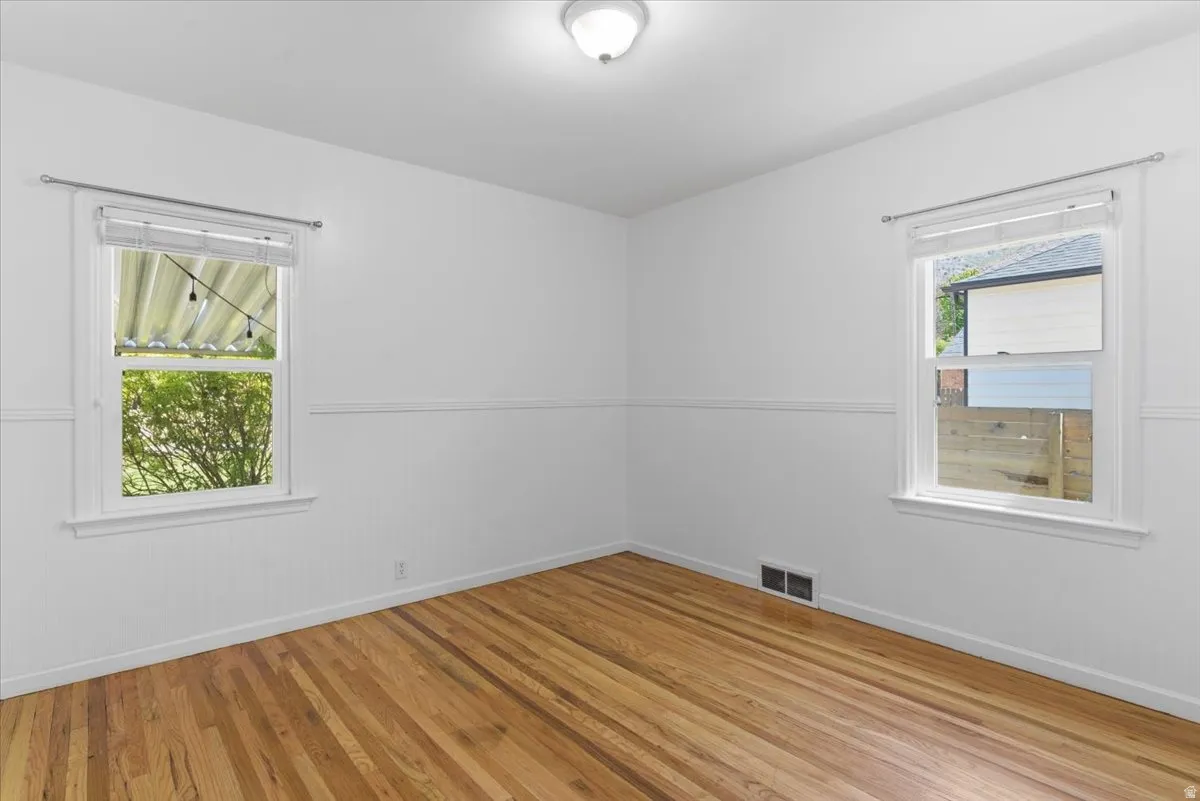 Room featuring wood-finish flooring, two windows with white trim, white wall paneling, and a flush-mount ceiling light fixture
