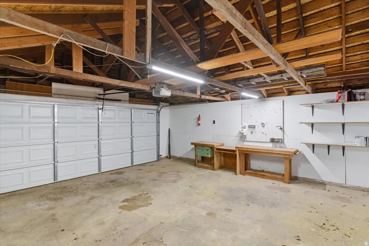 Spacious garage featuring a multi-panel overhead door, concrete flooring, exposed wood beam ceiling, built-in shelving, and workbench areas