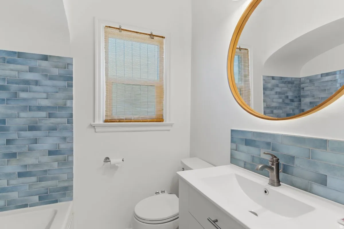 Bathroom featuring a vanity with an integrated sink, a circular back-lit mirror, and blue subway tile detailing