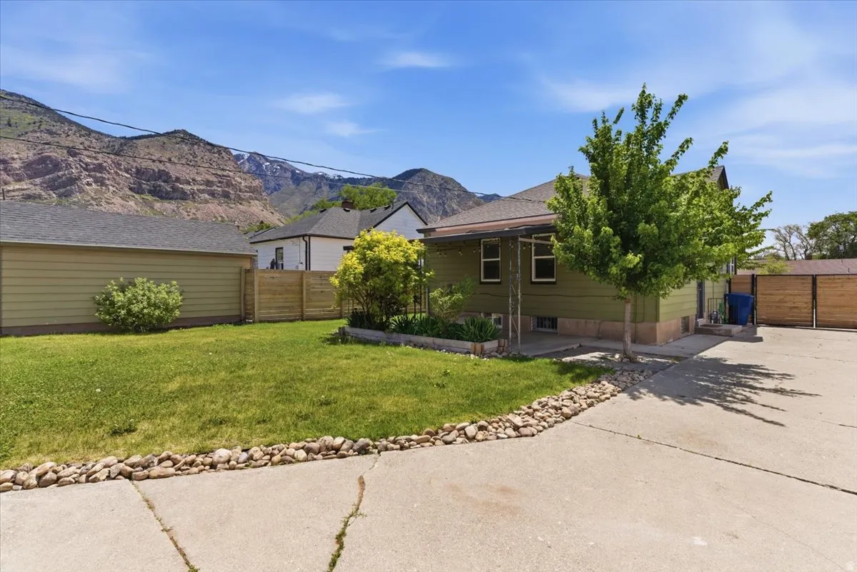 Property exterior featuring a green facade, paved driveway, detached garage with horizontal siding, wooden privacy fencing, and a mature tree
