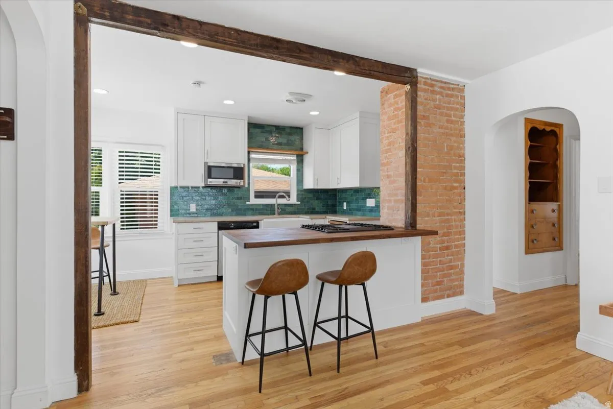 Open-concept kitchen featuring white cabinetry, a teal tile backsplash, recessed lighting, and a kitchen island with a wood-finish countertop