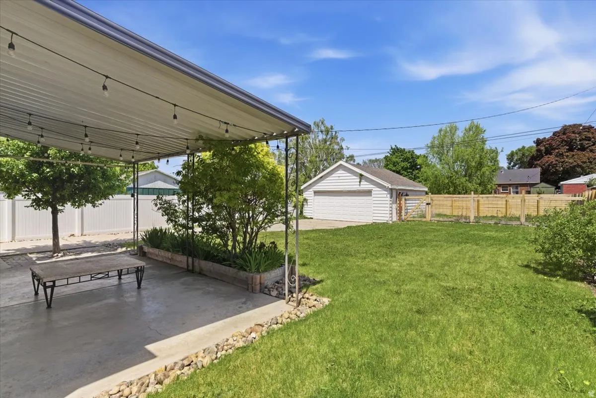 Expansive backyard featuring a covered patio with string lighting, mature trees, a detached two-car garage, and partial perimeter fencing