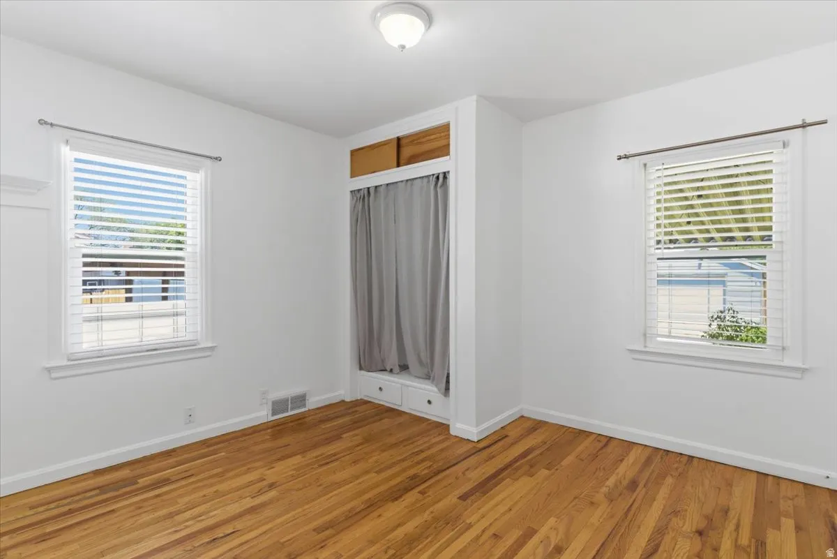 Wood-finish flooring, white painted walls, and two windows with blinds