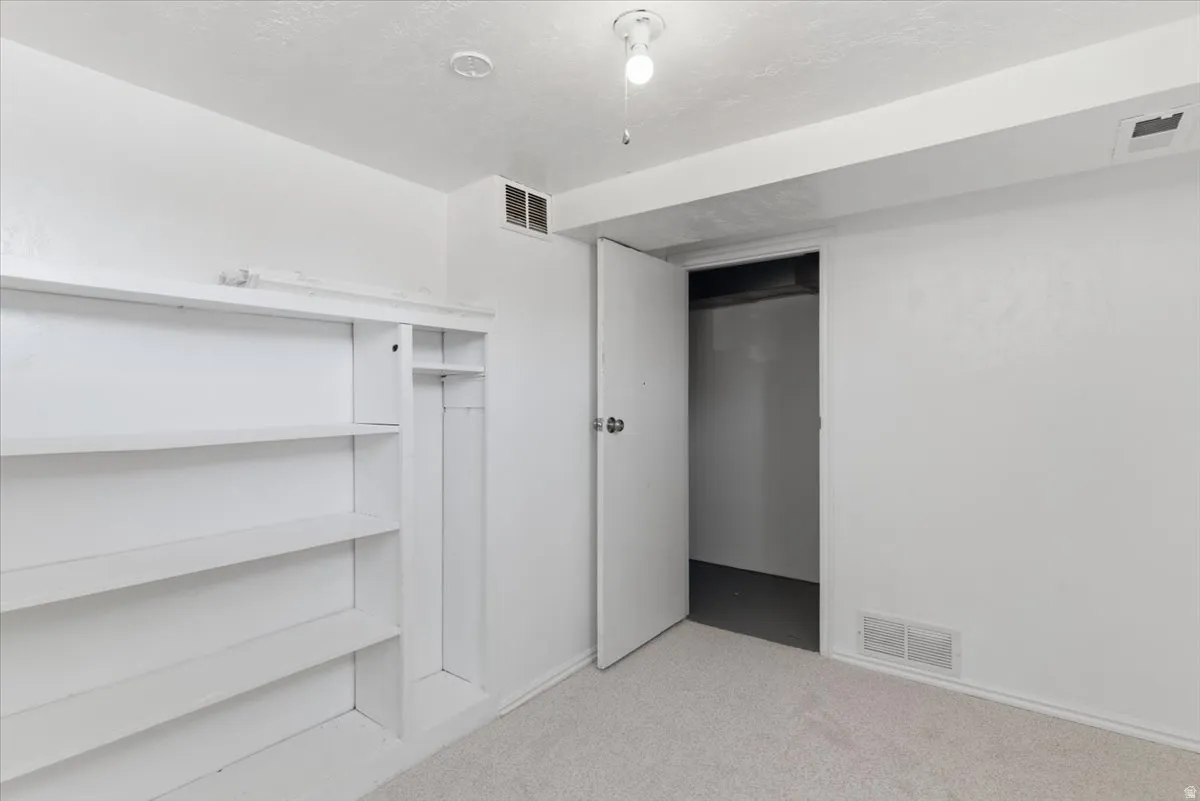 Room featuring light-toned carpet flooring, built-in shelving, and a white interior door