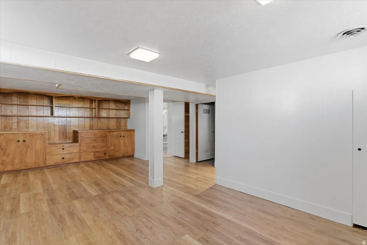 Spacious room featuring wood-finish flooring, a built-in wood cabinetry system with shelving and drawers, white walls, and a ceiling-mounted light fixture