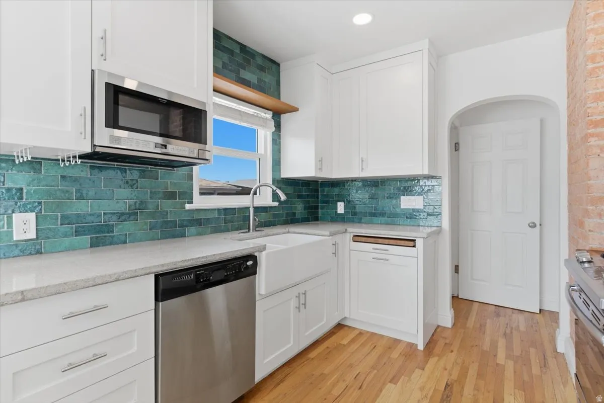Kitchen featuring white shaker cabinetry, stainless steel appliances, a farmhouse sink, light-toned countertops, and a full-height teal subway tile backsplash