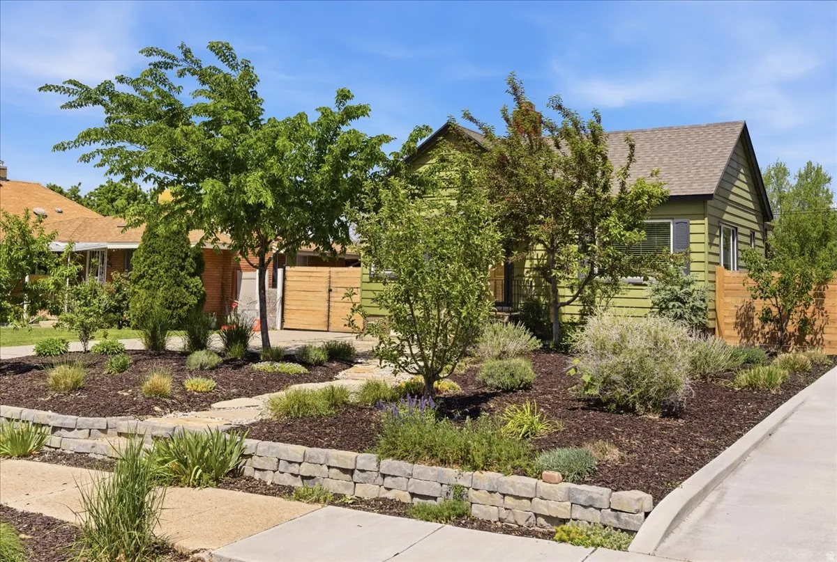 Landscaped front yard featuring a stone retaining wall, various plantings, and wood-finish fencing