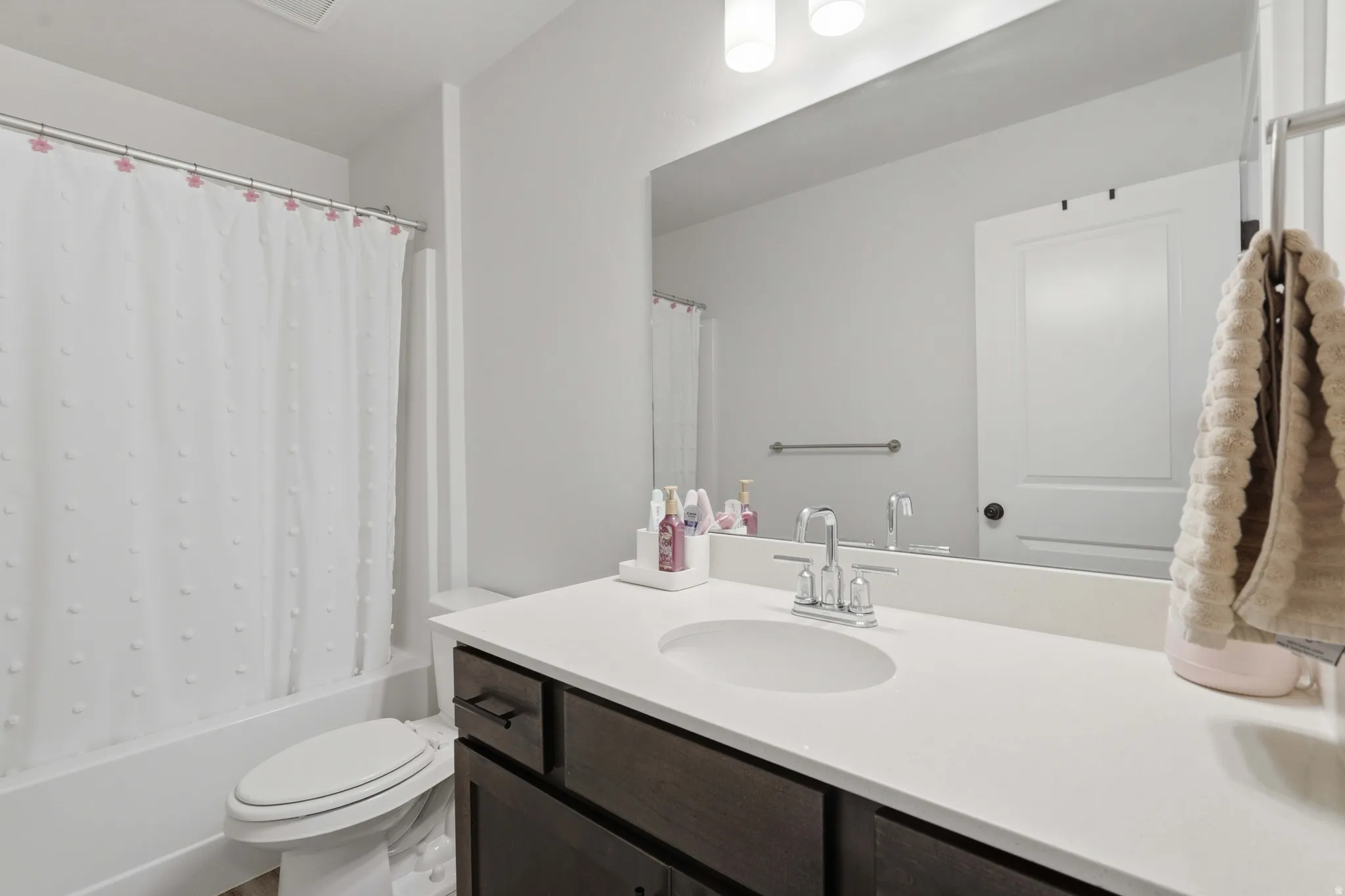 Bathroom featuring a white bathtub and toilet, a dark wood-finish vanity with a white countertop, a chrome faucet, and a large wall-mounted mirror