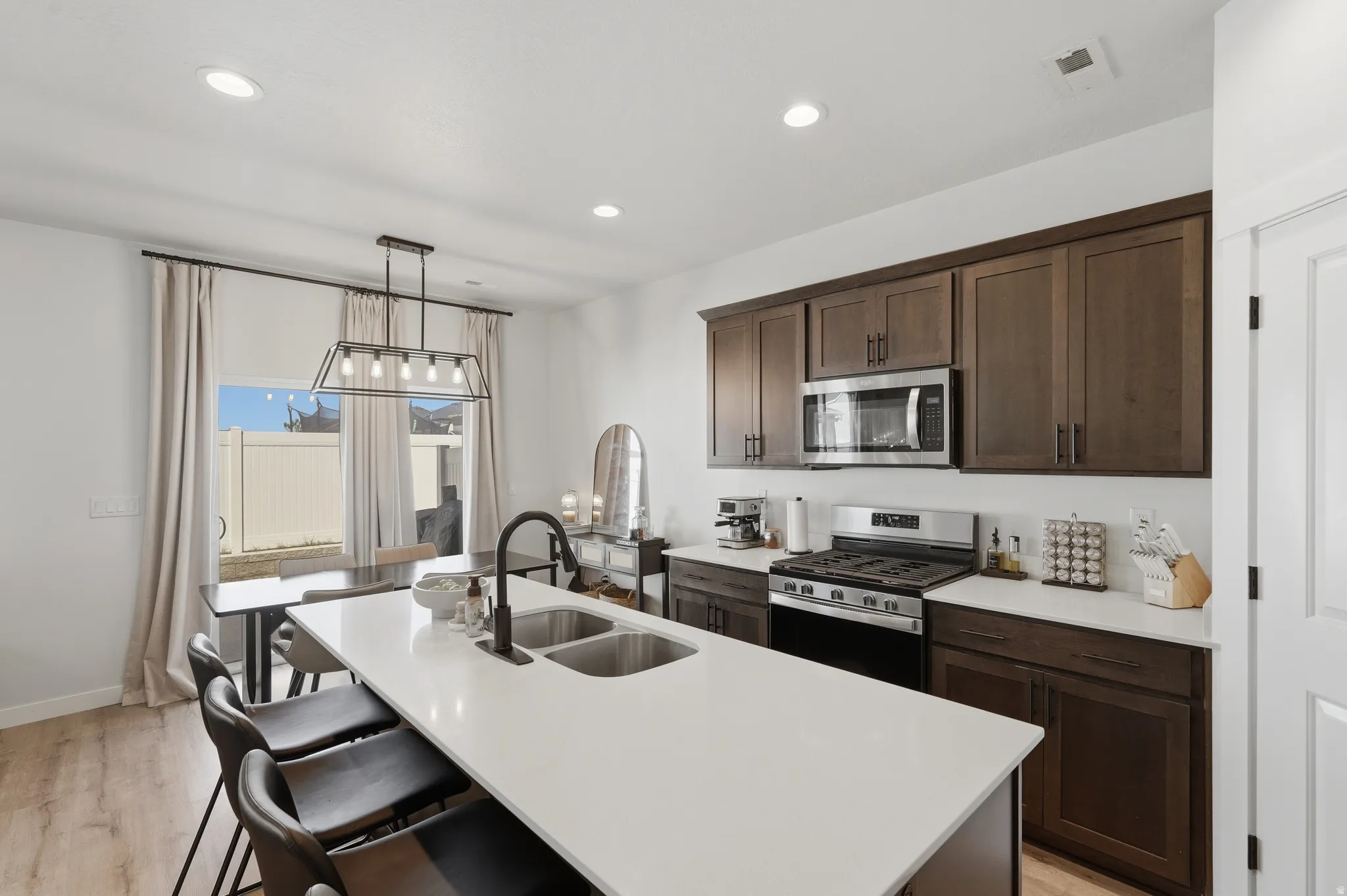 Bright kitchen featuring a central island with a double basin sink, dark wood-finish cabinetry, stainless steel appliances, a gas range, and wood-finish flooring