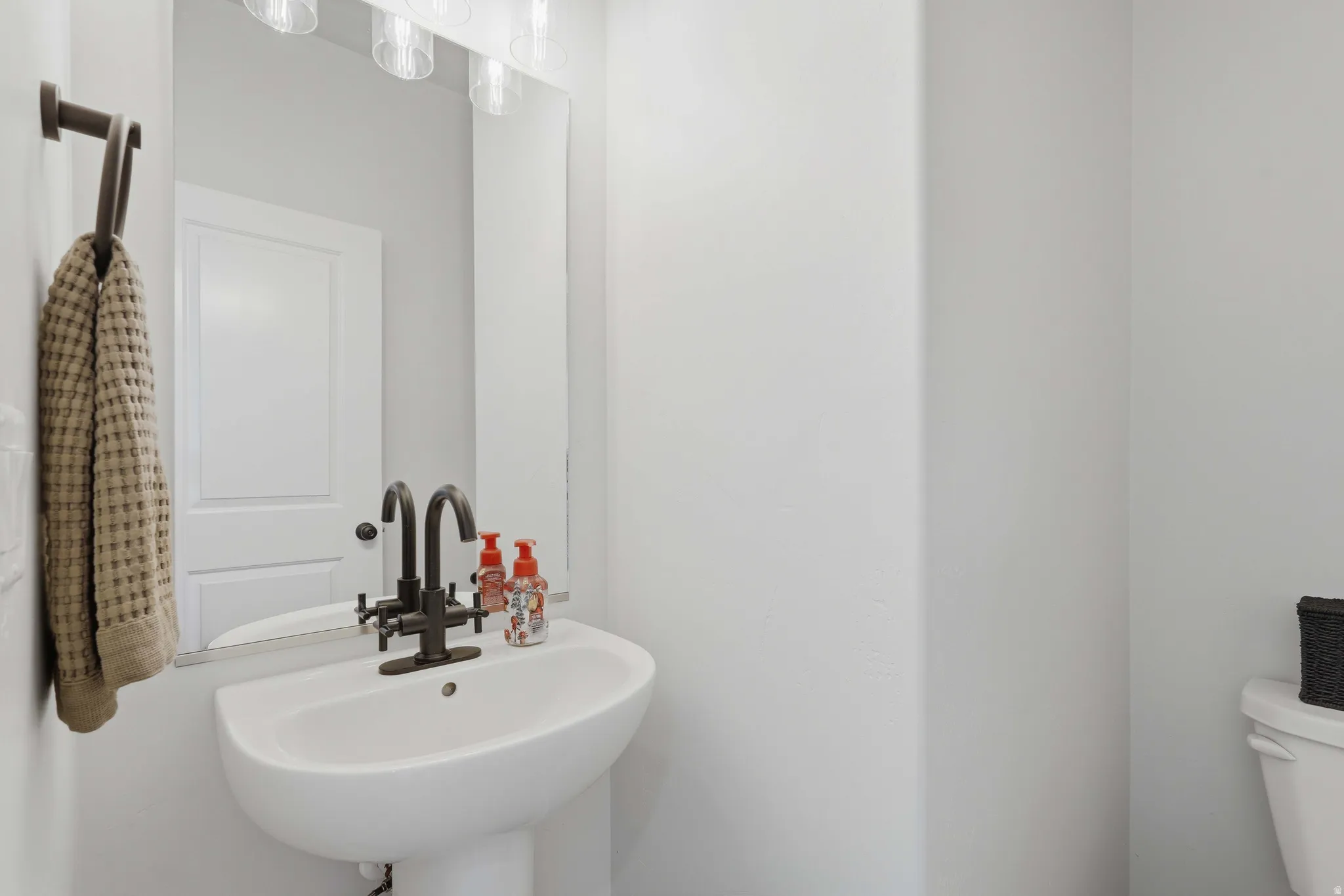 Pedestal sink featuring a contemporary bronze-finish faucet, rectangular wall mirror, and a three-light vanity fixture