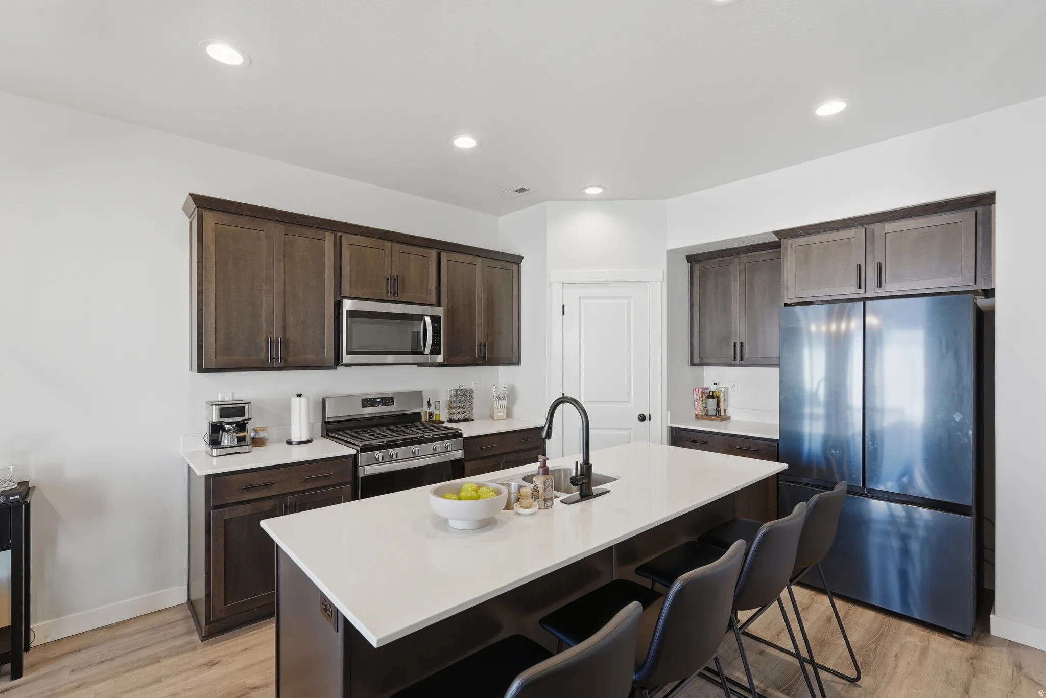 Kitchen featuring an expansive island with a matte black faucet, dark wood-finish cabinetry, stainless steel appliances, and white countertops