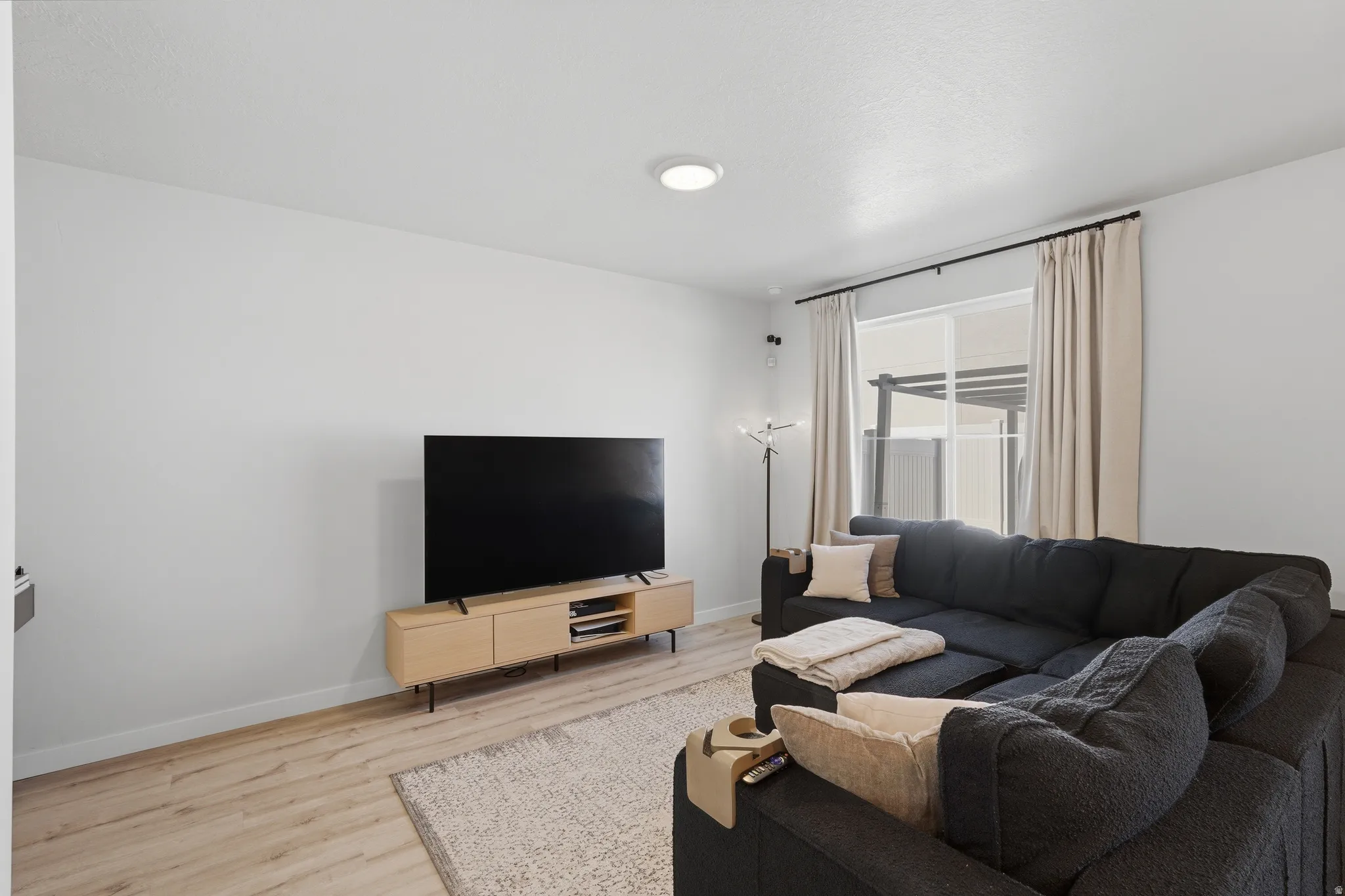 Bright interior space featuring light-colored walls, wood-finish flooring, and a large window with privacy blinds