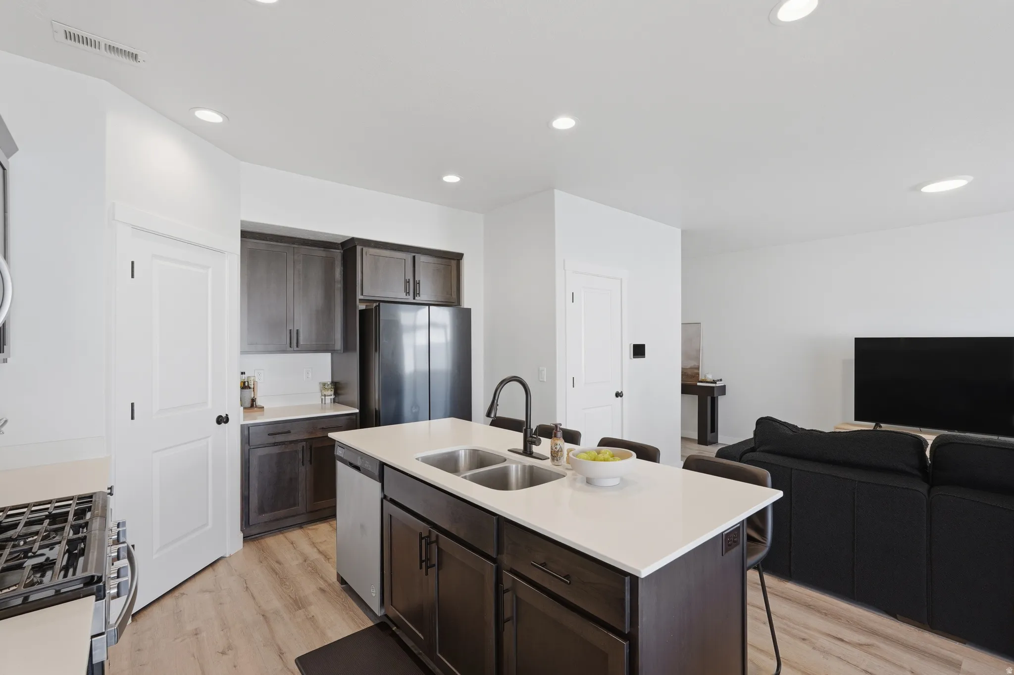 Kitchen featuring a central island with dual sinks, light-toned countertops, dark wood-finish cabinetry, stainless steel appliances, and wood-finish flooring