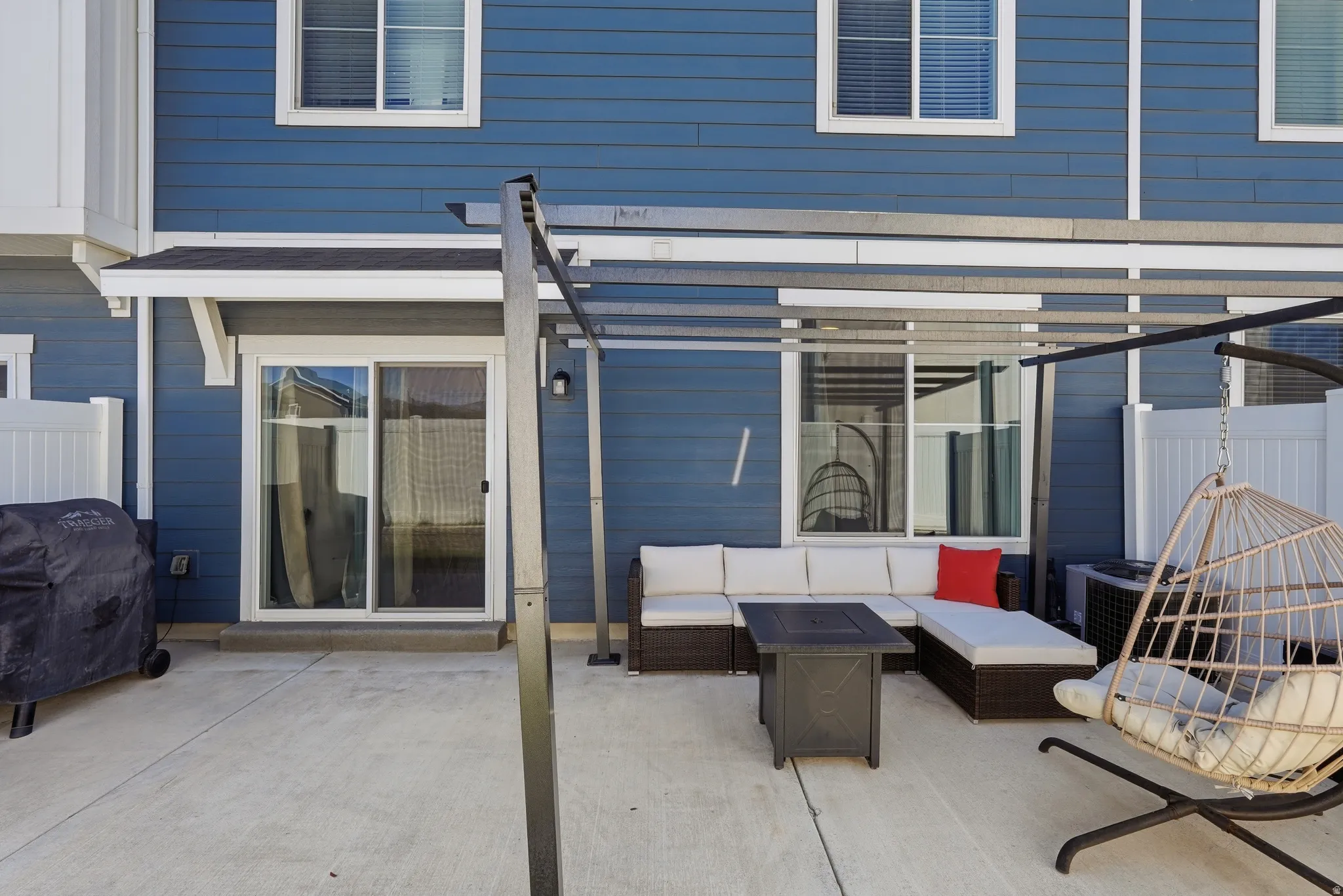 Private concrete patio featuring a modern pergola structure, blue siding, and white trim