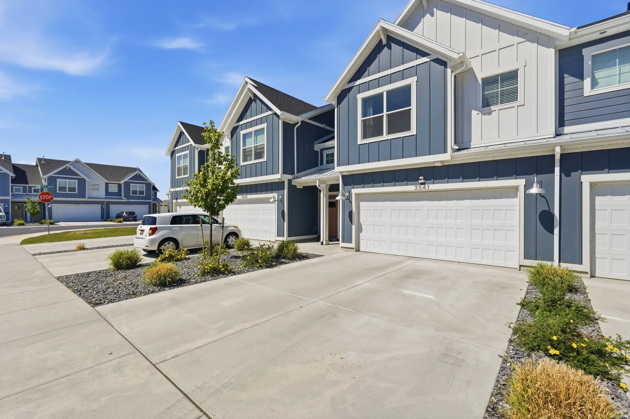 Modern townhome exterior featuring blue vertical siding, white board and batten accents, and white paneled garage doors
