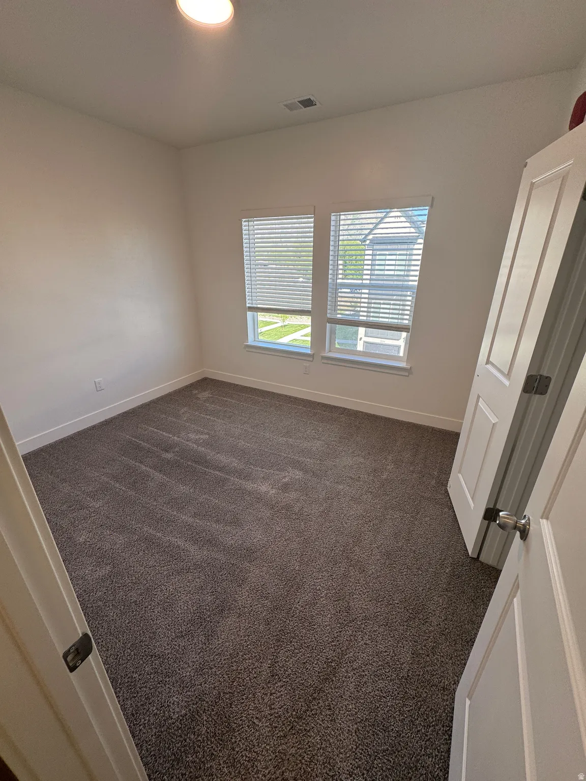 Neutral-toned carpeted interior space with two double-hung windows featuring horizontal blinds