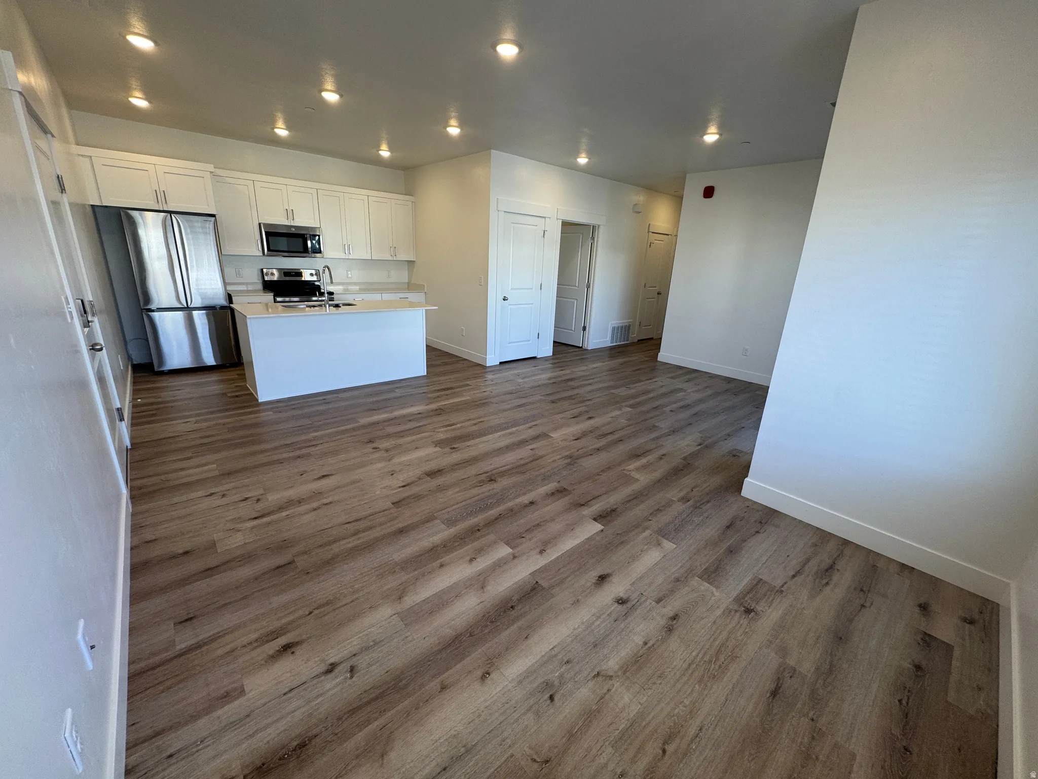Open-concept living space featuring wood-finish flooring, recessed lighting, and a kitchen with white cabinetry
