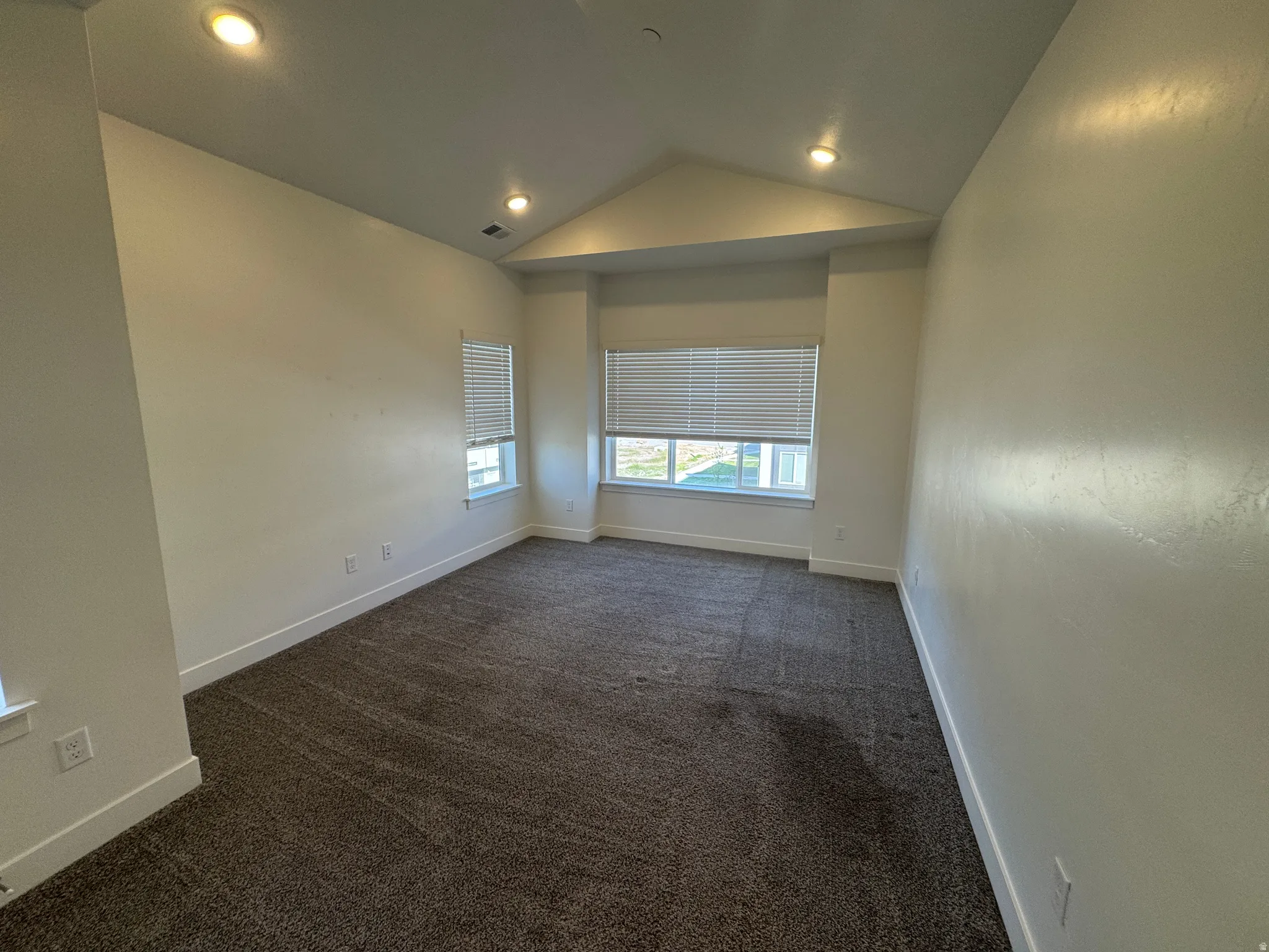 Carpeted room featuring multiple windows with blinds, recessed lighting, and a vaulted ceiling