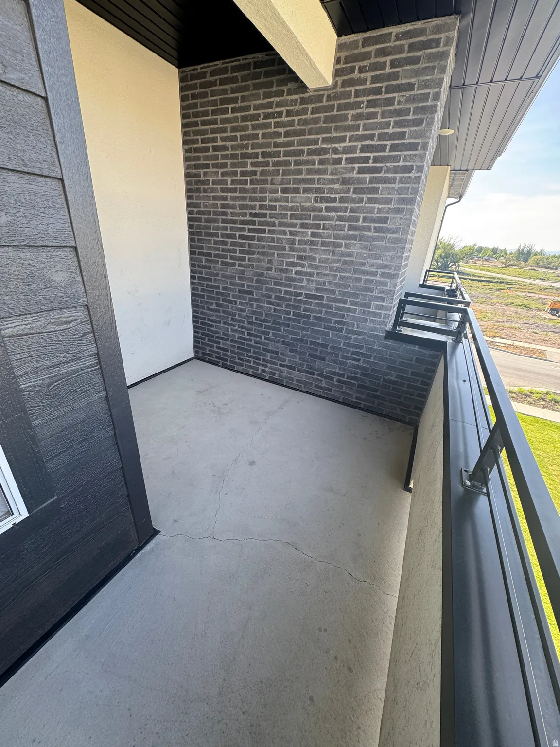 Outdoor balcony with concrete flooring, dark brick accent wall, and black metal railing