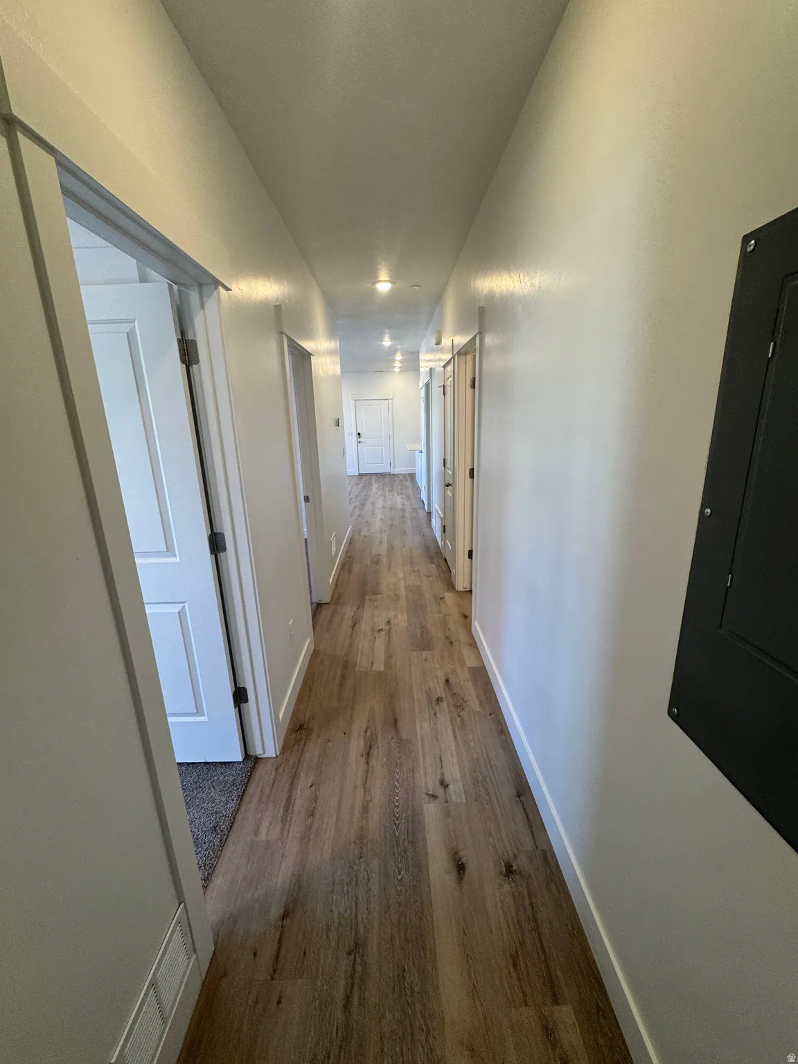 Hallway featuring wood-finish flooring, recessed lighting, white walls, and multiple panel doors