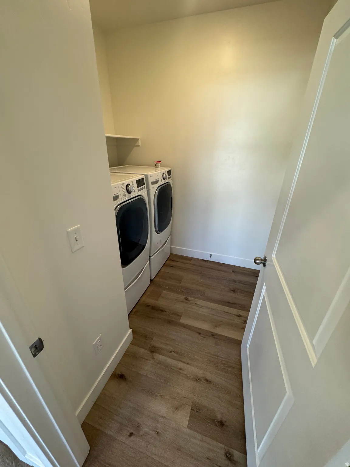 Dedicated laundry area featuring wood-finish flooring and a wall-mounted shelf