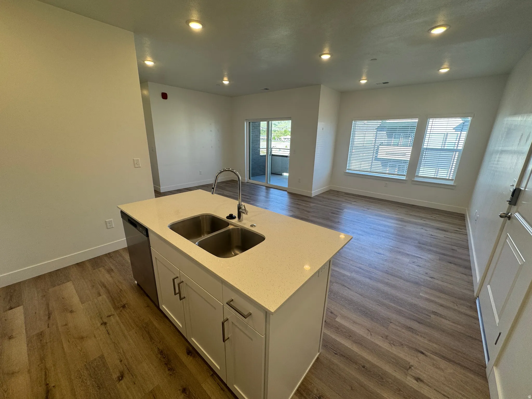 Kitchen island featuring a double-basin stainless steel sink with a high-arc faucet, white cabinetry, and a light-toned countertop
