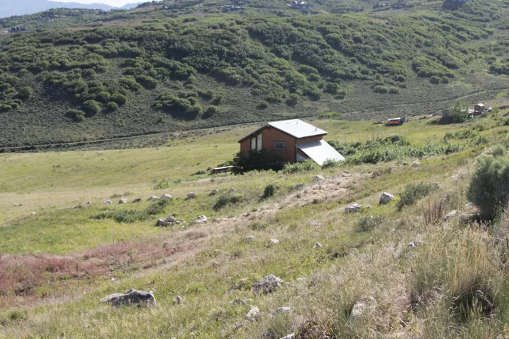 Brown-sided dwelling with a light-colored roof, positioned in a natural, expansive green and brown landscape