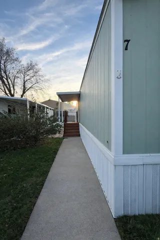 Property exterior featuring light green siding and white trim, with a concrete pathway leading to a covered entry with wood stairs