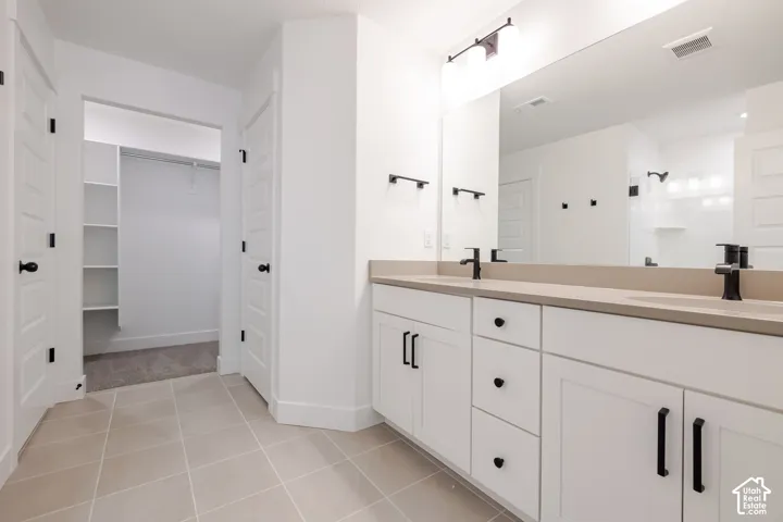 Dual vanity with matte black fixtures, extensive countertop space, white cabinetry, and large mirror
