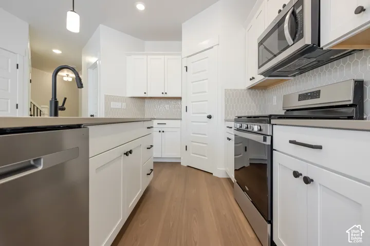 Kitchen featuring stainless steel appliances, white cabinetry, light countertops, wood-finish flooring, and a patterned tile backsplash