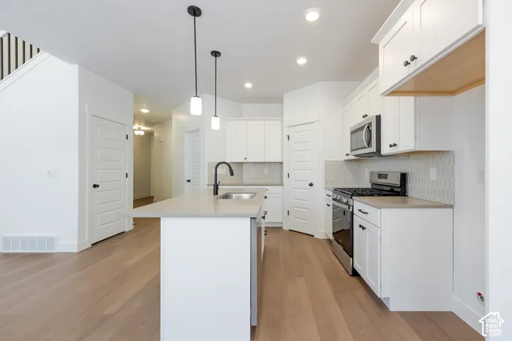 Kitchen featuring white cabinetry, stainless steel appliances, a center island with sink, and wood-finish flooring