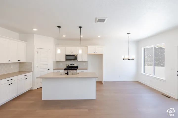 Kitchen featuring white cabinetry, stainless steel appliances, a center island with sink, and wood-finish flooring